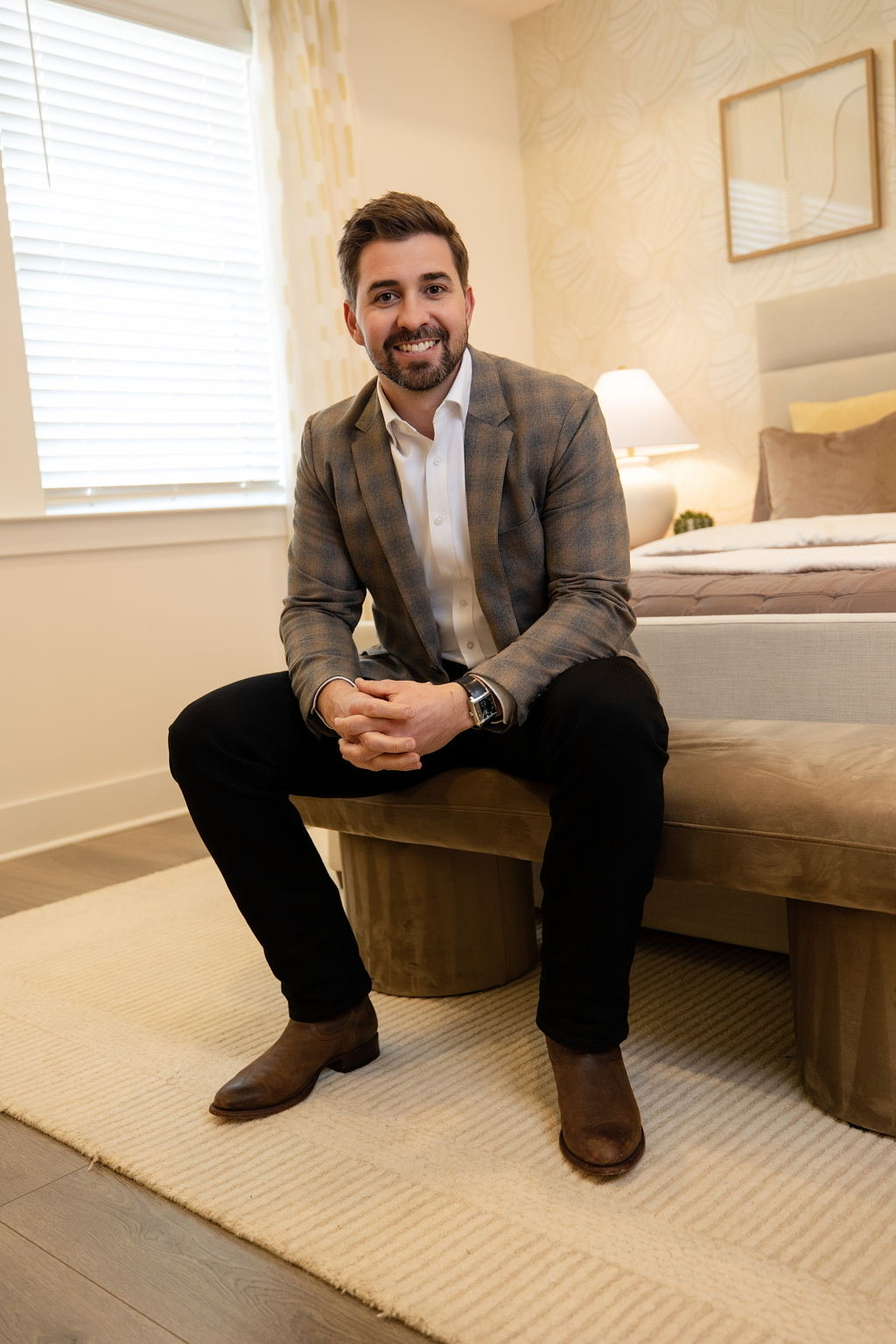 Cale Iorg seated in a warmly lit room, smiling, wearing a tan plaid blazer.